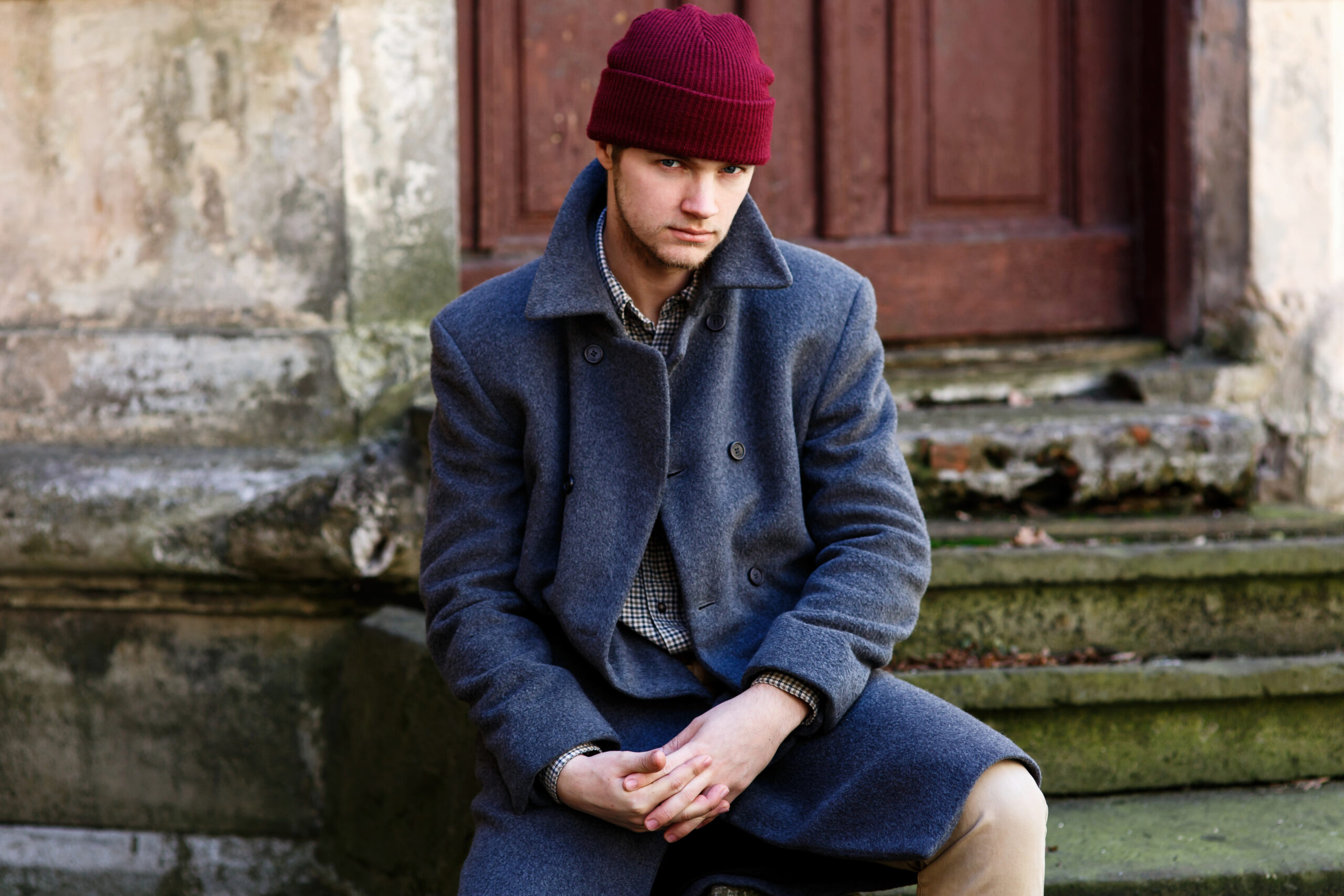 Young man in red hat and grey coat sits on ruined footsteps